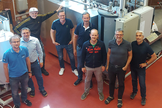 Eine Gruppe von acht Personen steht vor einem Speichersystem.