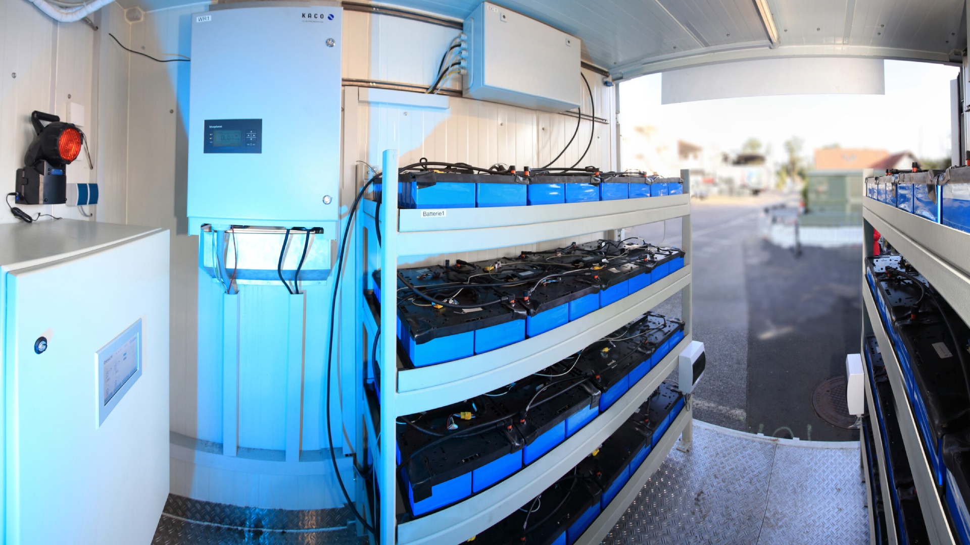 © Klimafonds/Krobath Container mit Regal, auf dem mehrere alte Antriebsbatterien von E-Fahrzeugen als stationärer Stromspeicher dienen