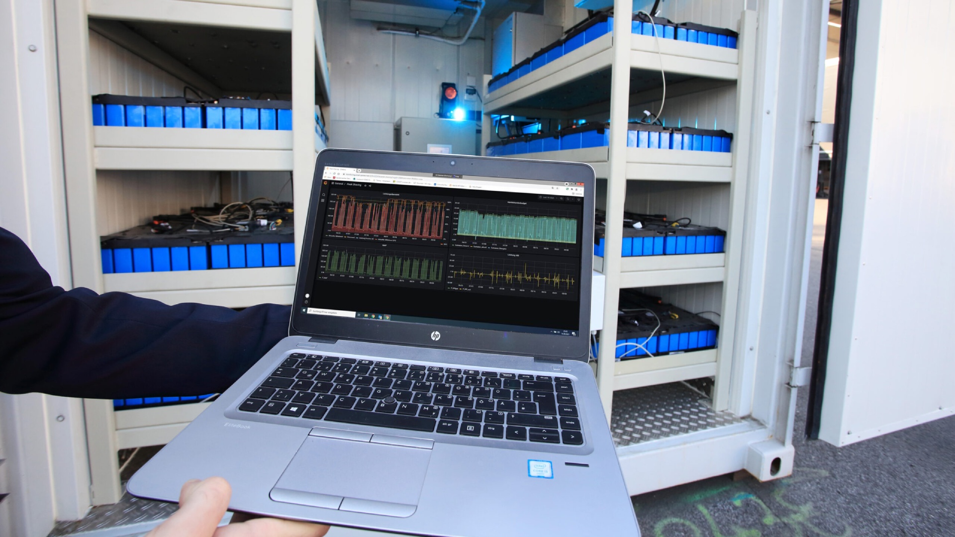 © Klimafonds/Krobath Ein Regal mit mehreren ausgebauten E-Auto-Batterien, davor ein Computer-Bildschirm, der die Regelung der Batterien zeigt