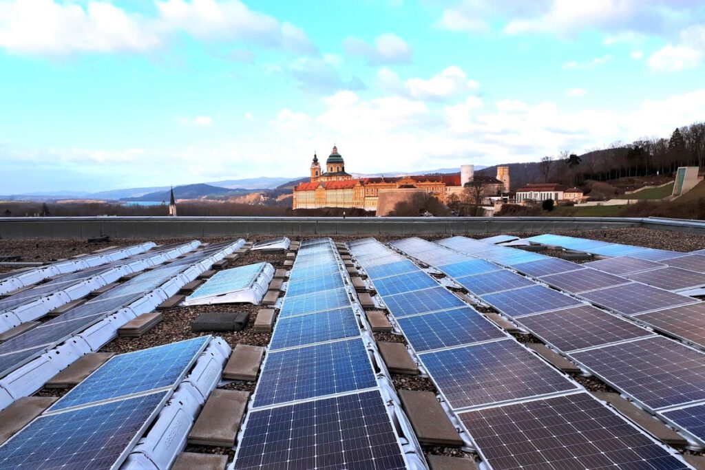 Photovoltaik-Anlagen auf einem Boden aus Steinen. Im Hintergrund sieht man ein Schloss und Hügel.