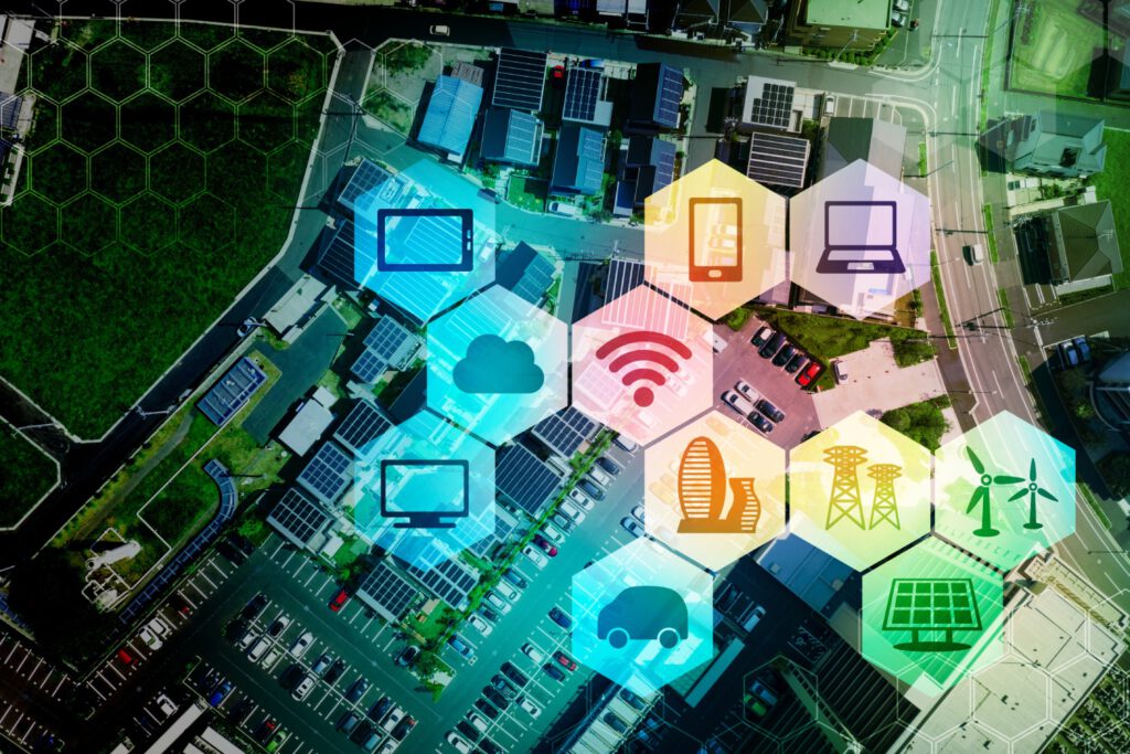Darstellung einer Stadt im Hintergrund und im Vordergrund werden Icons in Bienenwaben angezeigt (Laptop, Tablet, Smartphone, Bildschirm, WLAN-Zeichen, Windräder, Sonnenkollektor, Fahrzeug, Gebäude, Hochspannungsmast, Wolke)