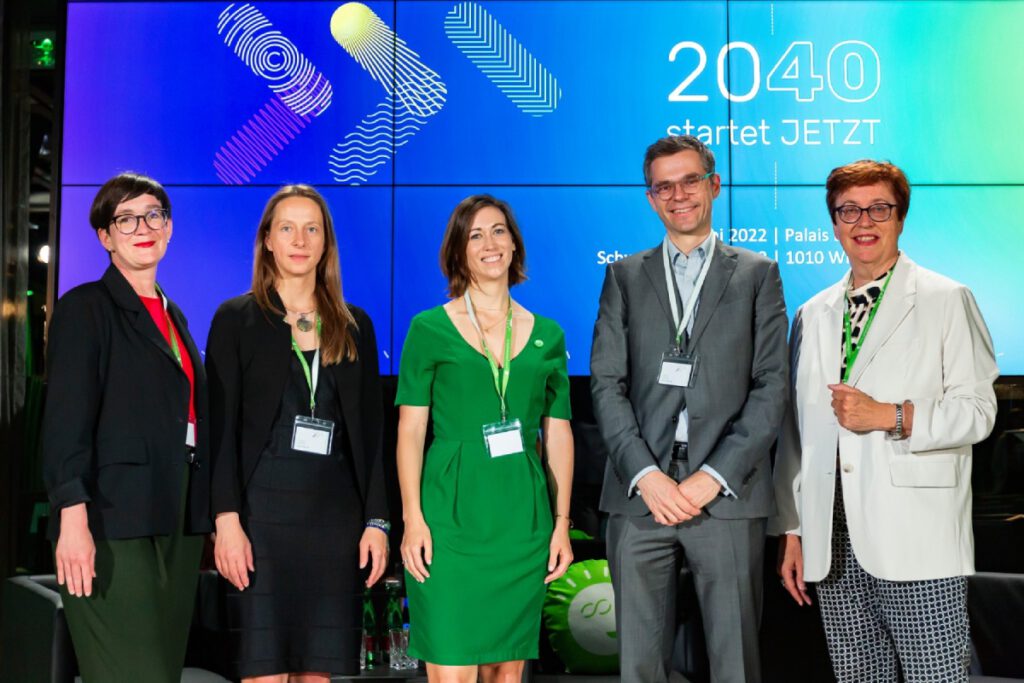 Fünf Personen stehen vor einem Bildschirm, auf dem eine Präsentation angezeigt wird.