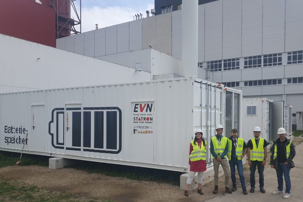 Fünf Personen mit Warnwesten stehen vor einem Batteriespeicher