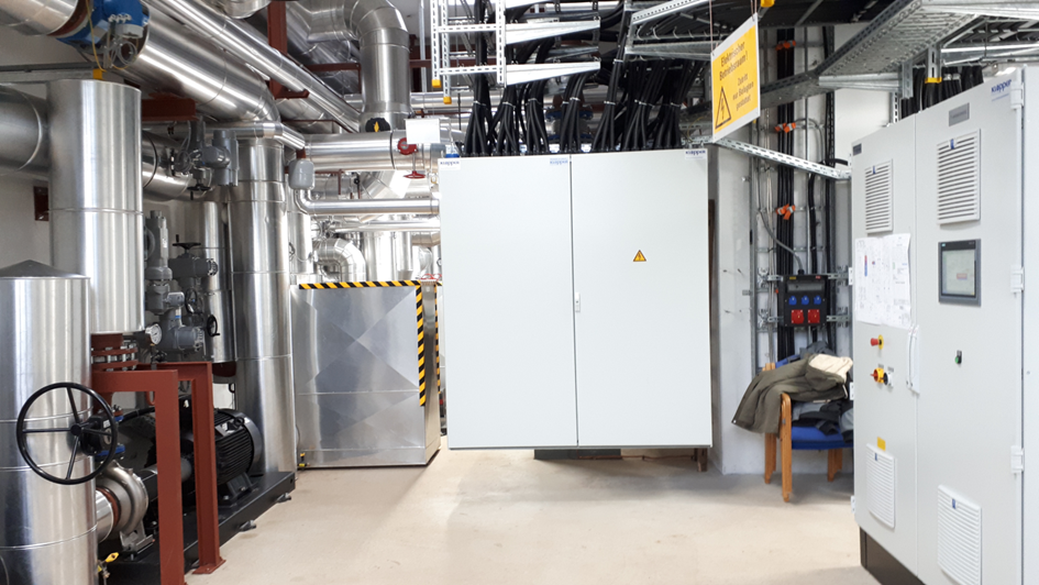 Technikraum mit Schaltschrankanlagen und verschiedenen Rohrleitungen (Innenraum einer Power2Heat-Anlage)