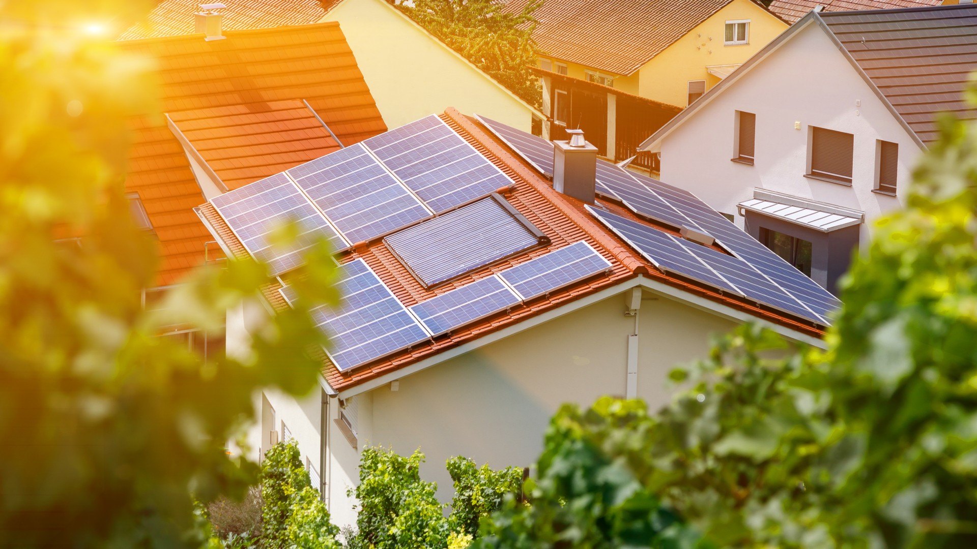 © iStock.com/Lari Bat Sonnenkollektoren auf dem Ziegeldach eines Gebäudes, von schräg oben durch Bäume hindurch aufgenommen