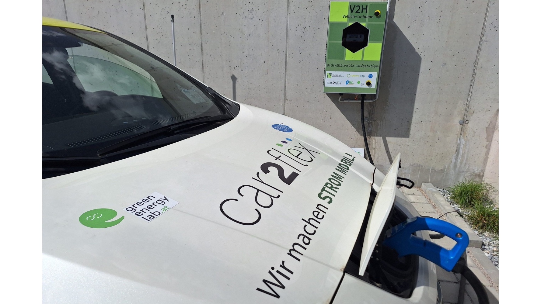 Ein E-Auto ist an einer bidirektionalen Ladesäule angesteckt. Nur die Motorhaube und die Windschutzscheibe des Autos sind sichtbar.
