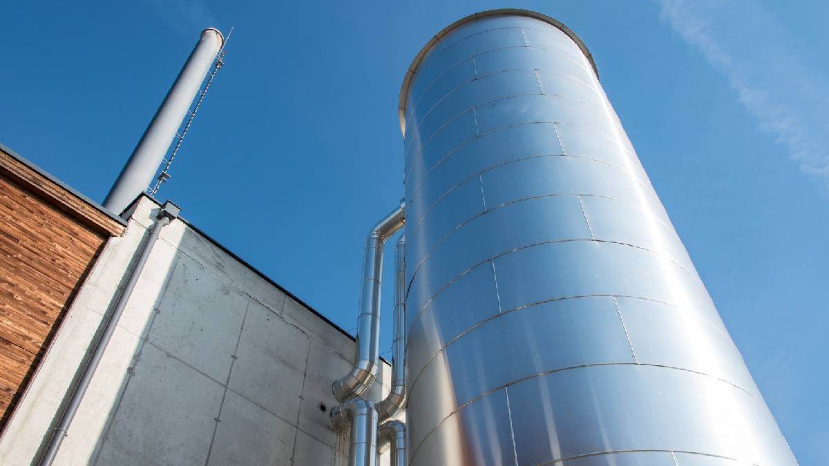 © 4ward Energy Research Ein großer silberfarbener Heizkessel ist über Rohre mit einem Gebäude verbunden, aus der Froschperspektive