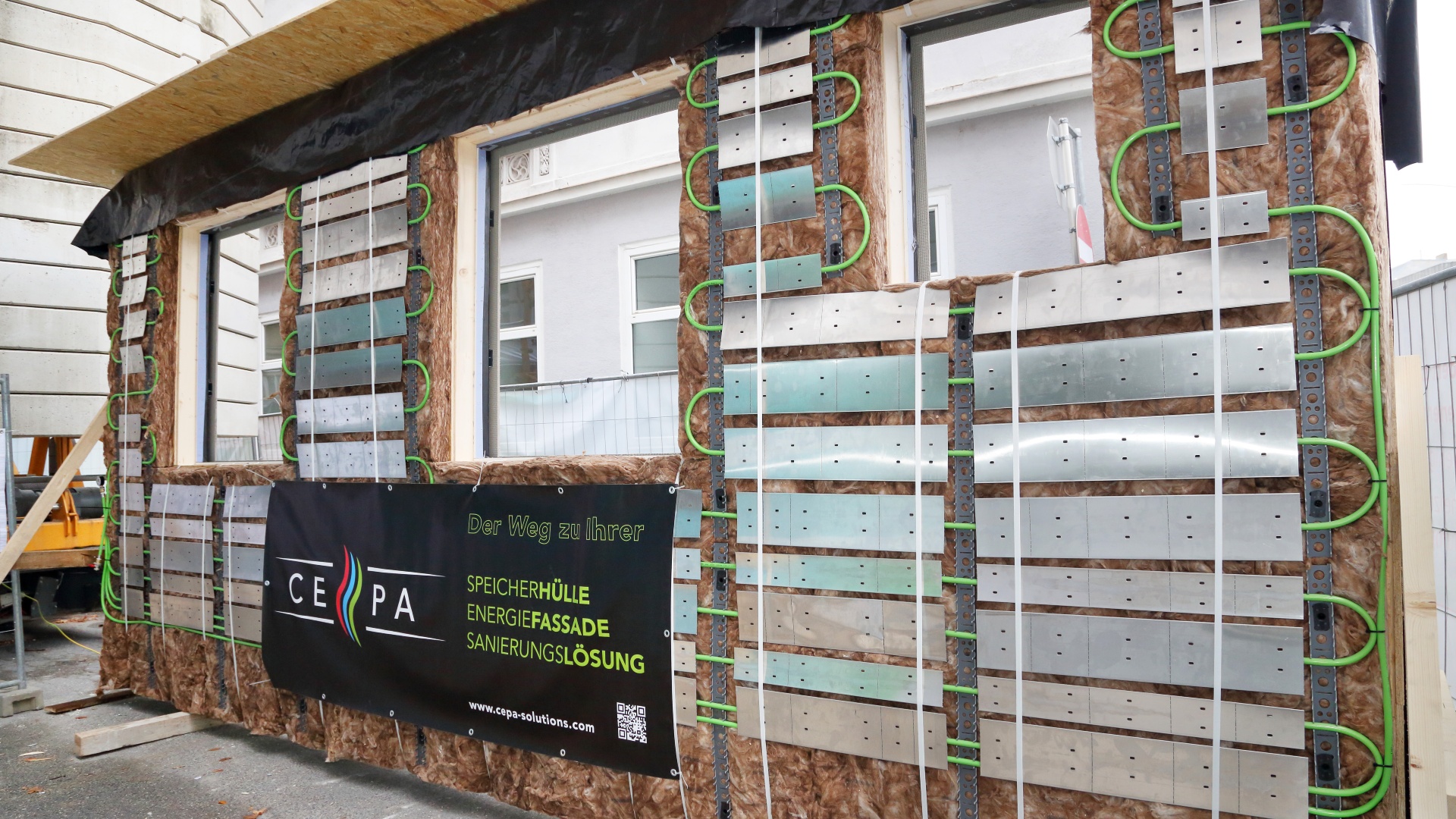 © Klimafonds / Krobath Außenwand im Bauzustand mit Dämmung, Metallplatten und grünem Kabel