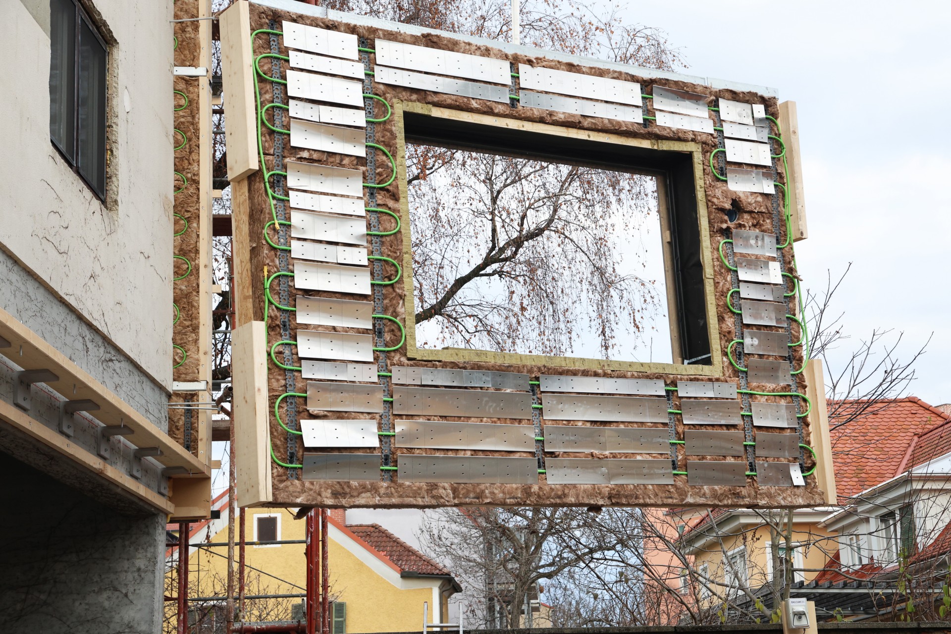 Ein vorgefertigtes Fassadenelement mit Holz, Dämmung und Metallplatten mit grünen Kabeln, in dessen Mitte ein Fenster vorgesehen ist.