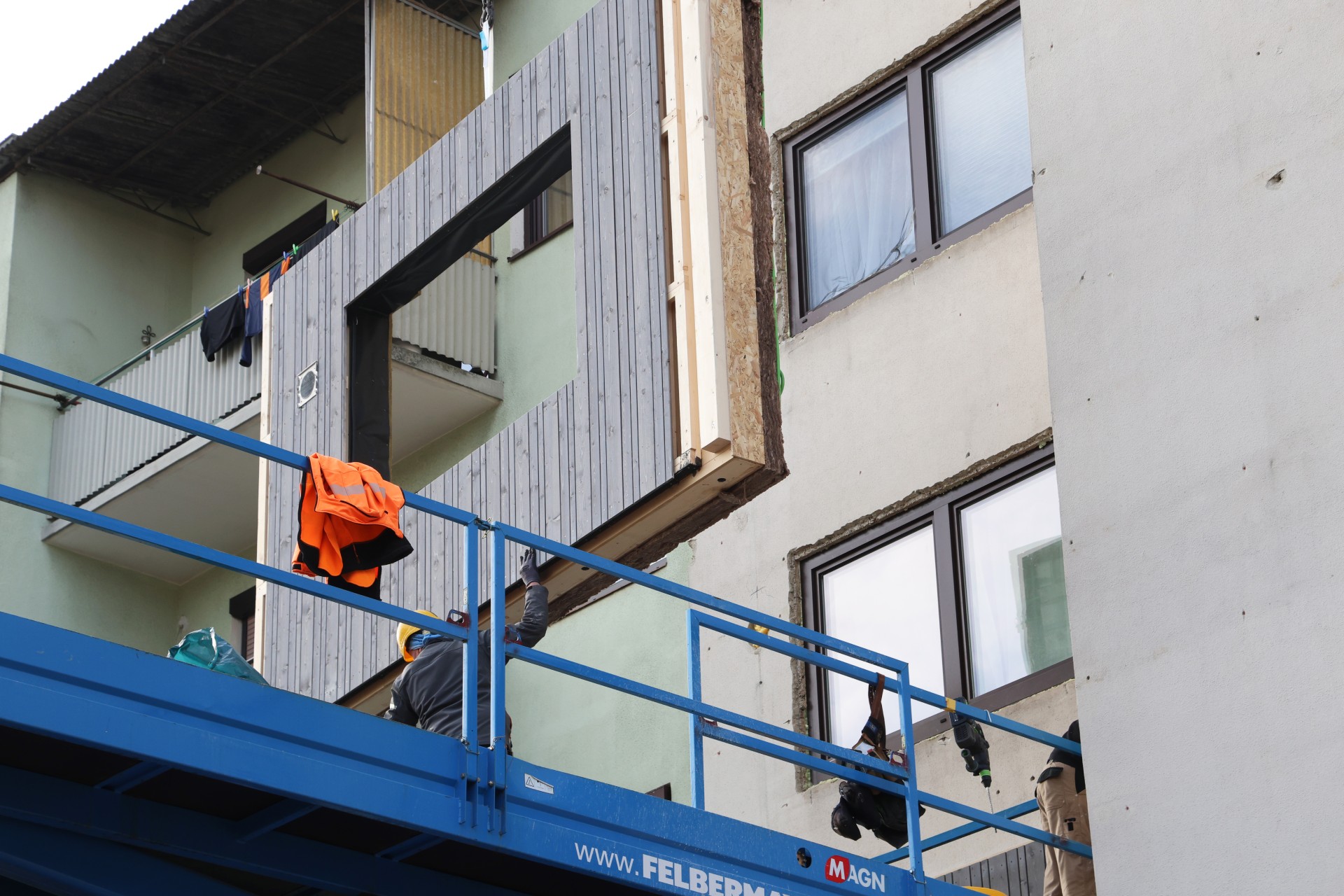 Ein vorgefertigtes Fassadenmodul wird an einem Kran an ein Gebäude im Bau angehoben.