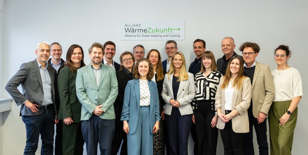 Gruppenfoto von siebzehn Personen. Im Hintergrund hängt ein Schild mit dem Logo der Allianz WärmeZukunft an der Wand.