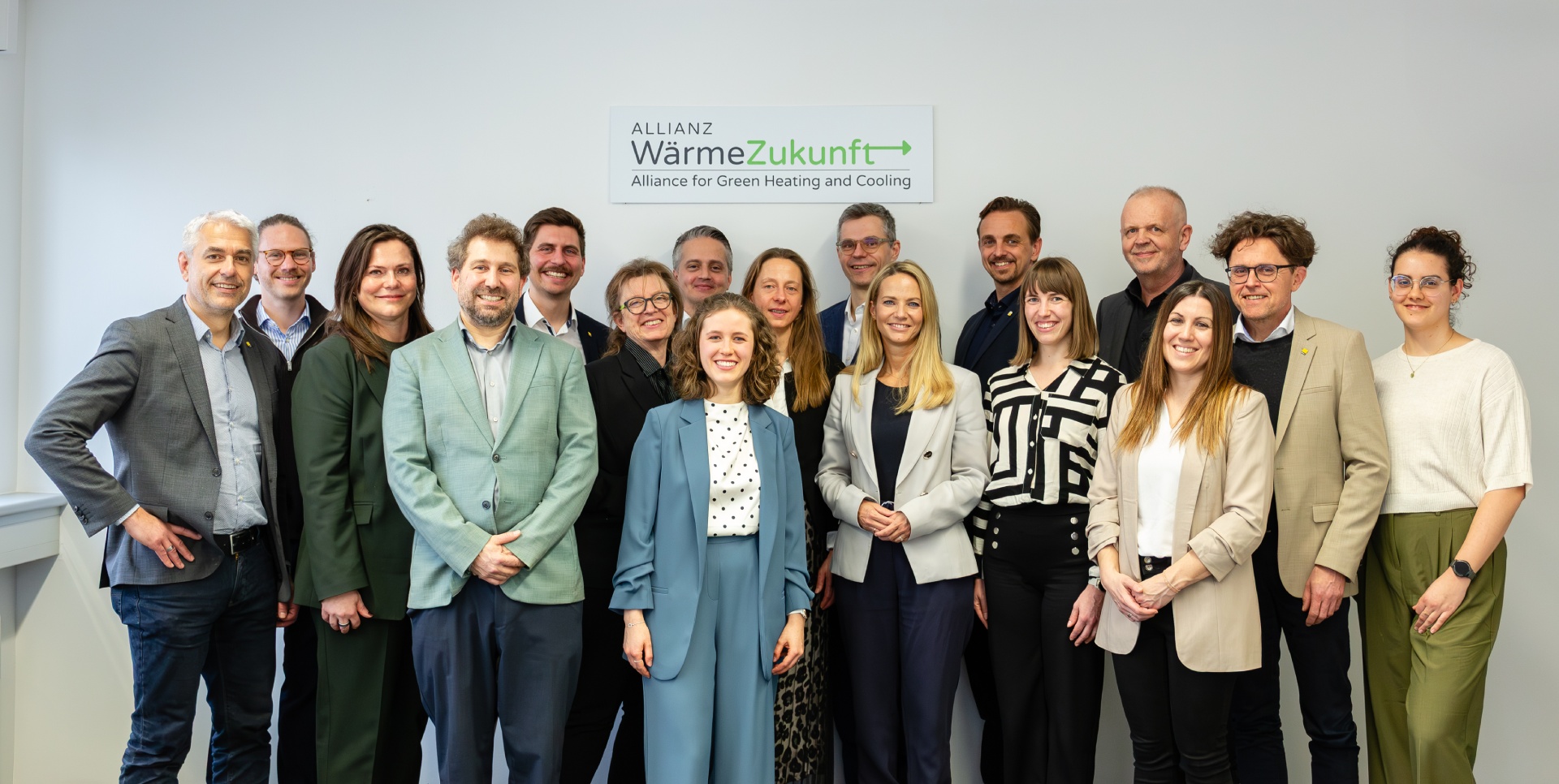 Gruppenfoto von siebzehn Personen. Im Hintergrund hängt ein Schild mit dem Logo der Allianz WärmeZukunft an der Wand.